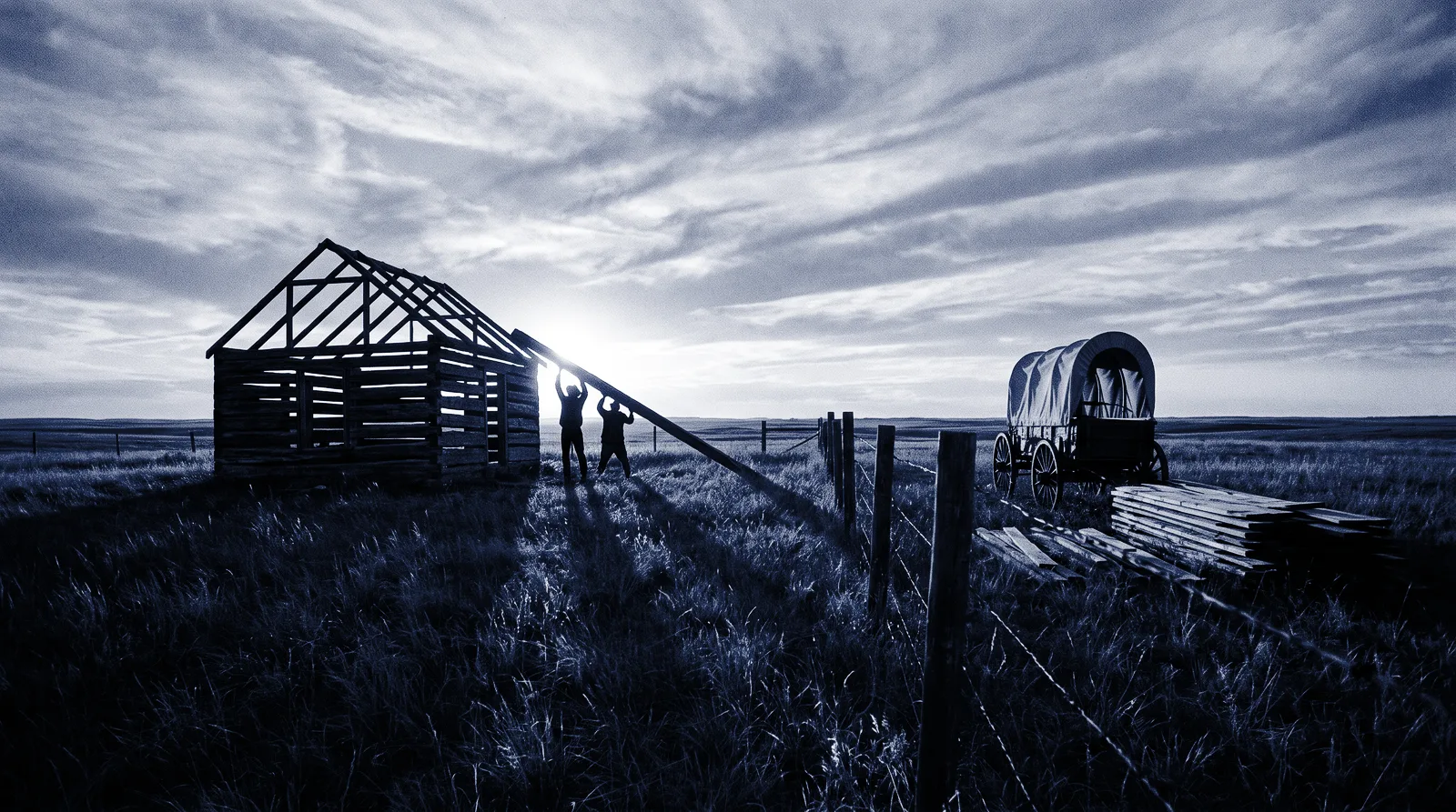 Settlers raising the frame of a homestead at sunset on claimed prairie land